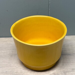 Puede incluir: Un cuenco de cerámica amarillo brillante. El cuenco tiene una forma redondeada con un acabado liso y brillante. El interior también es amarillo. El borde es ligeramente acampanado. Probablemente está destinado a uso decorativo o práctico.