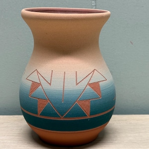 May include: A matte ceramic vase with a flared rim, featuring a gradient color transition from a light tan top to a deep teal base. The surface is decorated with etched geometric triangle patterns and horizontal lines revealing the terracotta clay.