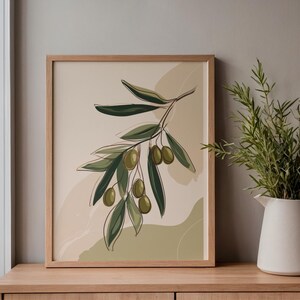 May include: A framed art print depicting an olive branch. The illustration features green olives and leaves in a minimalist line drawing style. The frame is made of light-coloured wood, and the background is a neutral beige.