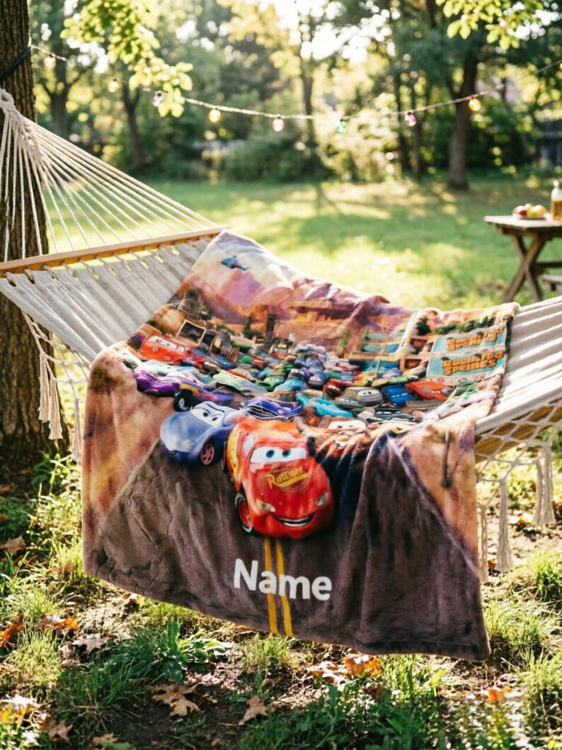 May include: A soft plush throw blanket featuring a colorful graphic print of various animated race cars from the movie Cars, including a prominent red race car in the foreground, with the word Name printed in white text on a road-like design.