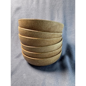 May include: A stack of six beige ceramic bowls. The bowls have a speckled texture and a simple, rounded design. The bowls are stacked on top of each other, with the rims facing upwards.