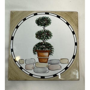 May include: Square ceramic tile featuring a decorative illustration of a topiary tree in a brown pot. The tree has three tiers of green foliage with red accents. The tile has a white center with a black and white border and a tan outer edge.