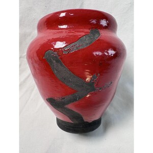 May include: A red ceramic vase with a glossy finish. The vase features a dark, abstract design across its surface. The base is a darker shade of red. The vase is a decorative item.