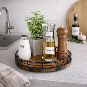 May include: A wooden serving tray with a black metal rim holds a white salt shaker, a small potted plant, a glass olive oil dispenser, and a wooden pepper grinder. The salt shaker has the word "Salt" printed on it.