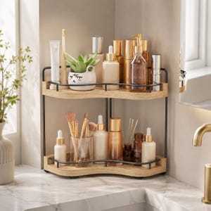 May include: A two-tier corner shelf with light wood-grain shelves and a black metal frame. The top shelf holds a toothbrush, a small white planter with a face, and various skincare bottles. The bottom shelf contains makeup brushes and bottles.