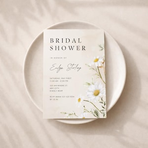 May include: A bridal shower invitation with the words "BRIDAL SHOWER" at the top. The invitation features a watercolor design with daisies and the text "IN HONOR OF Eulga Stirling". The invitation is on a white plate.