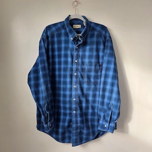 May include: A blue plaid button-down shirt with long sleeves, a chest pocket, and a button-down collar. The shirt is made of a soft, woven fabric and is hanging on a white hanger.