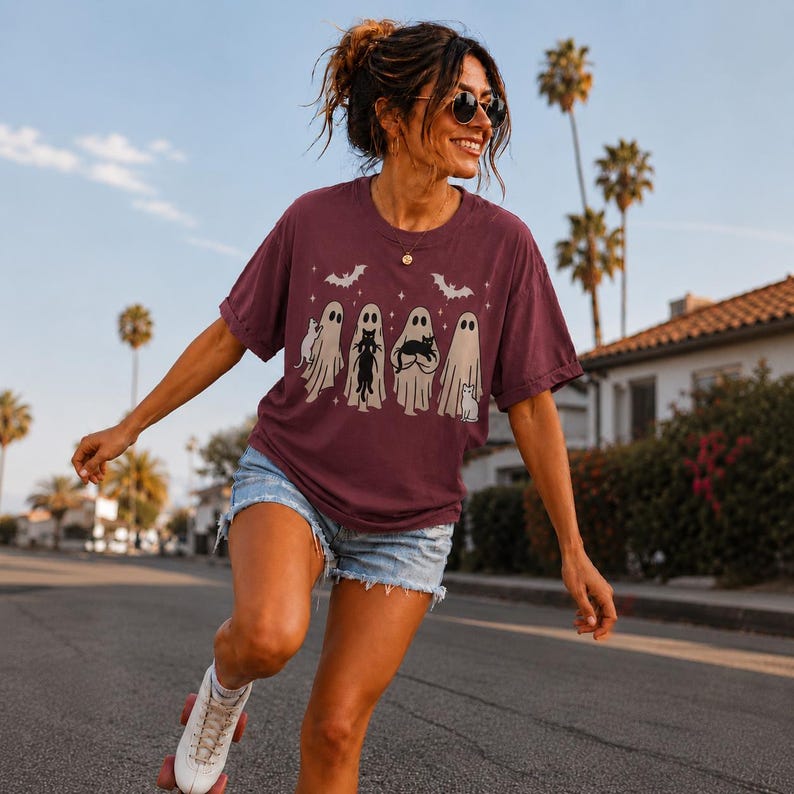 Pu&ograve; includere: Una t-shirt a maniche corte color bordeaux con una stampa grafica di quattro fantasmi beige e diversi gatti neri. Il design include piccole stelle bianche e due pipistrelli in volo. La maglietta ha un girocollo e una vestibilit&agrave; ampia.