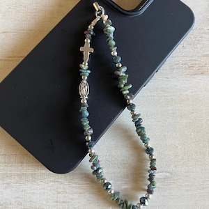 May include: A beaded phone charm with green and blue stones, silver beads, and a silver cross and Virgin Mary charm. The charm is attached to a black phone case.