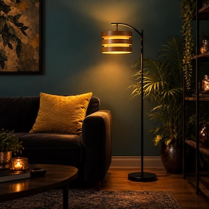 May include: A floor lamp with a thin black metal stand and a circular base, featuring a cylindrical shade made of three stacked horizontal wooden bands that emit a warm, glowing light from the center, illuminating the surrounding area.