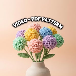 Könnte beinhalten: Ein Strauß bunter, gehäkelter Blumen in einer cremefarbenen Vase. Die Blumen sind in Rosa, Gelb, Blau, Grün und Lila gehalten. Der Text "VIDEO + PDF PATTERN" ist über den Blumen zu sehen.