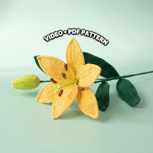Puede incluir: Un lirio amarillo tejido a ganchillo con hojas y un capullo verdes. La flor tiene estambres marrones y está sobre un fondo verde claro. El texto en la imagen dice "VIDEO + PDF PATTERN".