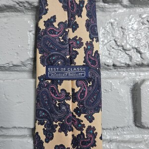 Peut inclure: Cravate Robert Talbott avec un fond crème et un motif cachemire répété bleu marine et magenta. L'étiquette indique "BEST OF CLASS®" et "Robert Talbott".