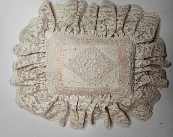 Cojín decorativo vintage de encaje color crema melocotón con medallón floral y ribete con volantes.