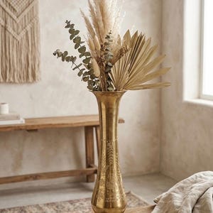 May include: A decorative gold vase with an etched design, holding dried pampas grass, eucalyptus, and palm leaves. The vase is on a wooden table. The arrangement has a neutral colour palette, creating a bohemian aesthetic. The vase is approximately 60 cm tall.