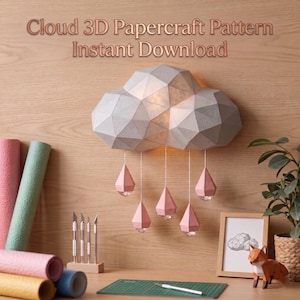 Puede incluir: Una lámpara de nube de papel con colgantes de gotas de lluvia rosas cuelga de una pared de madera. La lámpara está iluminada. La imagen incluye el texto "Cloud 3D Papercraft Pattern Instant Download". También se ven rollos de papel, una esterilla de corte y un zorro.