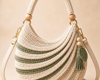 Puede incluir: Un bolso de ganchillo en forma de media luna de color crema con rayas verde salvia. Cuenta con un asa redondeada con cuentas de madera, herrajes de metal dorado, una correa de hombro desmontable y una borla decorativa verde salvia con una hoja.
