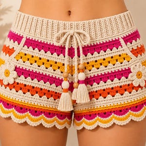 May include: Crochet shorts featuring a high-waisted ribbed band with a drawstring closure, adorned with two large floral appliques on the sides. The garment displays horizontal stripes in cream, bright pink, orange, and yellow with a scalloped hem.