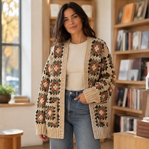 Può includere: Un cardigan a maniche lunghe aperto sul davanti con un motivo all'uncinetto a piastrelle granny nei toni del crema, verde salvia e terracotta. Il capo presenta due tasche applicate sul davanti e polsini a coste, indossato sopra un top color crema.