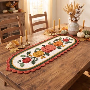 Puede incluir: Un camino de mesa ovalado de ganchillo con un centro color crema que presenta un patrón de enredadera con calabazas naranjas, rojas y amarillas y hojas verdes. Tiene un borde interior verde oscuro y un borde exterior festoneado color óxido.