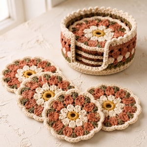 May include: A set of round, crocheted coasters featuring a floral pattern in shades of cream, terracotta, and olive green. The coasters are arranged in a matching circular crocheted holder with a scalloped edge, showcasing intricate yarn work.