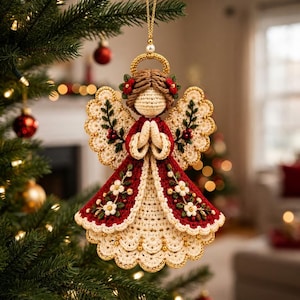 Pu&ograve; includere: Un angelo decorativo all'uncinetto con un abito color crema e uno strato rosso scuro, decorato con fiori bianchi ricamati e foglie verdi. La figura ha capelli castani, un'aureola dorata e mani giunte in preghiera, appesa a un cordino dorato.