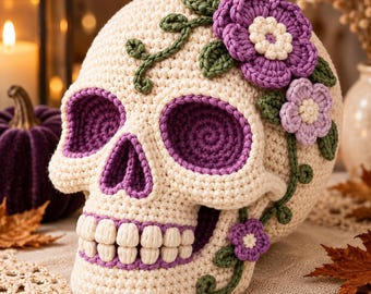 May include: A cream-colored crocheted skull featuring deep purple eye sockets and nasal cavity. The skull is decorated with crocheted green vines, dark purple flowers with cream centers, and smaller light purple flowers. The teeth are cream-colored.