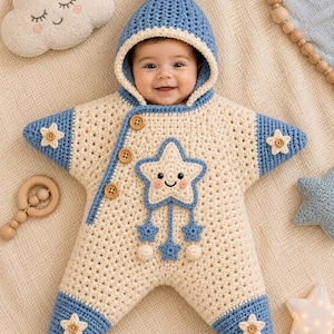 Peut inclure: Une gigoteuse en crochet en forme d'étoile, couleur crème et bleu, avec une capuche et un pompon. Elle présente des boutons en bois, une application d'étoile souriante avec des breloques étoiles pendantes et de petits motifs étoilés.