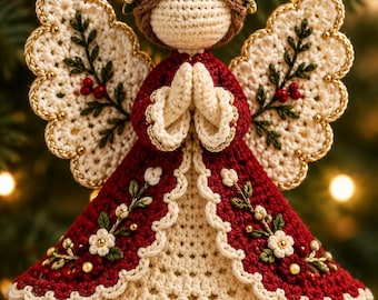 Puede incluir: Un adorno de ángel de ganchillo con un vestido rojo oscuro, bordados florales color crema y detalles de cuentas doradas. El ángel tiene cabello de hilo marrón, un halo dorado y alas color crema con bordados de hojas verdes y bayas rojas.