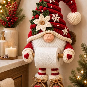 Könnte beinhalten: Ein gehäkelter Toilettenpapierhalter in Form eines Wichtels mit roter Mütze, weißem Bart und braunen Stiefeln. Der Wichtel ist mit einem weißen Weihnachtsstern, grünen Stechpalmenblättern und kleinen weißen Schneeflocken verziert und hält eine Rolle.