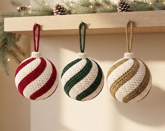 Puede incluir: Tres adornos esféricos de ganchillo con rayas diagonales en rojo, verde oscuro y dorado, alternando con hilo color crema. Cada adorno tiene un lazo de cuerda trenzada a juego para colgar y una tapa de ganchillo de color crema.