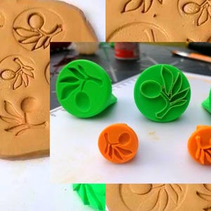 May include: Three bright green and two orange circular stamps featuring an embossed olive branch design. The stamps are shown alongside a tan clay slab with multiple circular impressions of the same olive branch pattern pressed into the surface.
