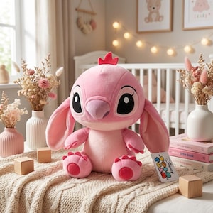 Può includere: Un peluche rosa di Angel con grandi occhi neri, orecchie lunghe e una cresta rossa. La bambola è seduta su una coperta color crema, con blocchi di legno e vasi di fiori secchi nelle vicinanze. Un'etichetta Disney Tsum Tsum è attaccata.