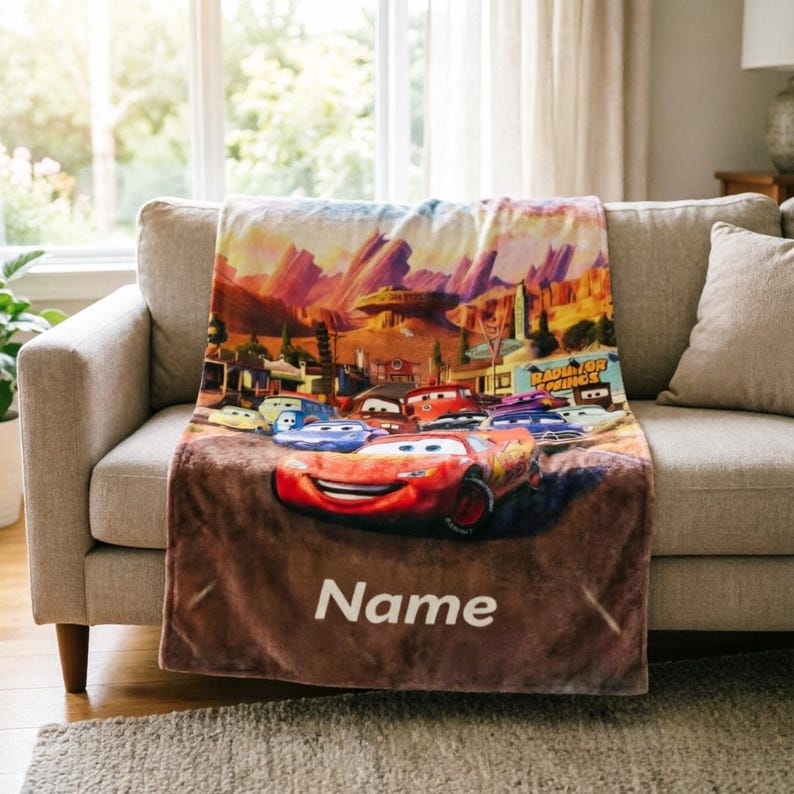 May include: A soft fleece blanket featuring a colorful graphic print of various animated race cars from the movie Cars, set against a desert landscape with the text Radiator Springs and the customizable word Name printed in white at the bottom.