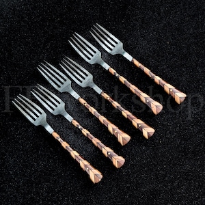 Può includere: Sei forchette con rebbi in acciaio inossidabile e manici in legno dal design complesso. I manici presentano un motivo geometrico di legno chiaro e scuro, con accenti in ottone. Le forchette sono disposte diagonalmente su una superficie scura.