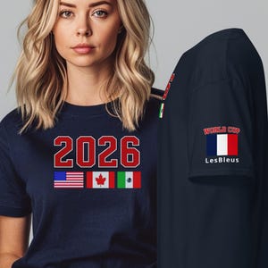 May include: Navy blue t-shirt with the number "2026" in red and white, along with the flags of the United States, Canada, and Mexico. The sleeve features the text "WORLD CUP" and the words "Les Bleus" with the French flag.