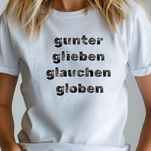 Może przedstawiać: Biała koszulka z nadrukiem słów "gunter, glieben, glauchen, globen" czarną, postarzaną czcionką. Koszulka wykonana jest z miękkiego materiału i ma krótkie rękawy.