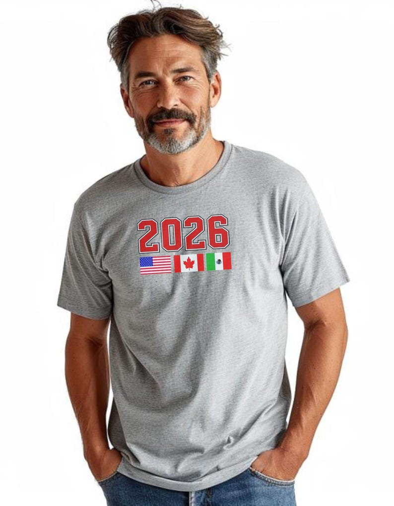 May include: A gray t-shirt with the number "2026" in red block letters. Below the number are the flags of the United States, Canada, and Mexico. The shirt is short-sleeved and has a crew neck.