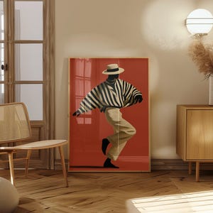 May include: A framed wall art print featuring a stylised illustration of a person wearing a wide-brimmed hat, a black and white striped long-sleeve shirt, and light-coloured trousers, set against a solid, vibrant red background.