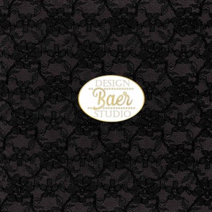 K&ouml;nnte beinhalten: Schwarzer Spitzenstoff mit einem goldenen ovalen Logo mit der Aufschrift "DESIGN Baer STUDIO".