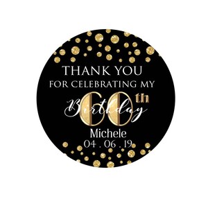 May include: A black and gold round sticker with the text "THANK YOU FOR CELEBRATING MY 60th BIRTHDAY Michele 04.06.19." Gold glitter dots are scattered around the edge. The number 60 is in gold with a gold border.