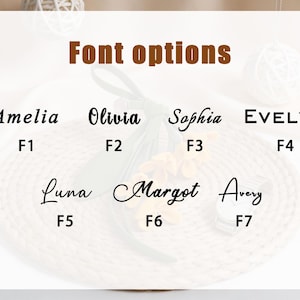 May include: A chart titled Font options displaying seven distinct typography styles labeled F1 through F7. The names Amelia, Olivia, Sophia, Evelyn, Luna, Margot, and Avery are written in black ink, showcasing various cursive and block letter fonts.
