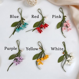 May include: Six decorative floral charms featuring green stems and leaves with small blossoms in blue, red, pink, purple, yellow, and white. Each charm includes a loop for hanging and is labeled with its corresponding color name in black text.