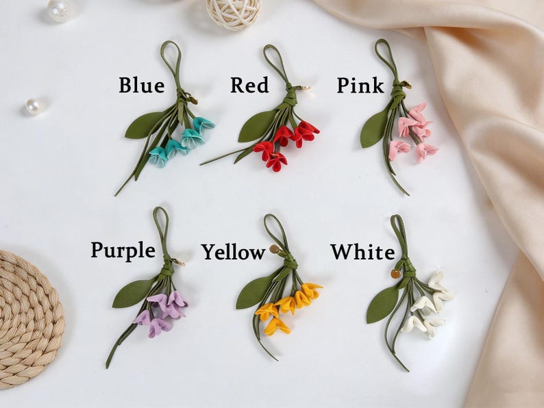 May include: Six decorative floral charms featuring green stems and leaves with small blossoms in blue, red, pink, purple, yellow, and white. Each charm includes a loop for hanging and is labeled with its corresponding color name in black text.