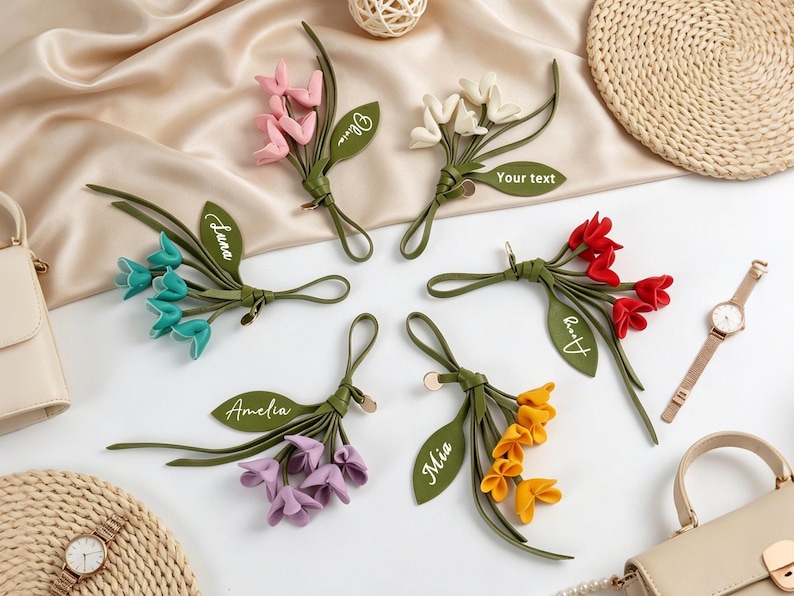 May include: Six decorative flower-shaped bag charms made of leather-like material in pink, white, teal, red, purple, and yellow. Each charm features a green leaf with custom text including names like Olivia, Luna, Amelia, Mia, Avery, and Your text.