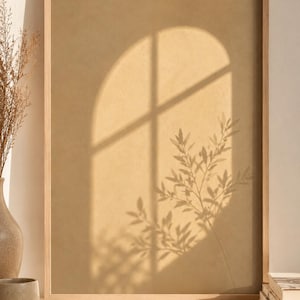 May include: A rectangular wall art print in a light-toned wooden frame. The print features a solid beige background with a projected shadow of an arched window and a leafy plant branch, creating a soft, layered effect of light and dark tones.