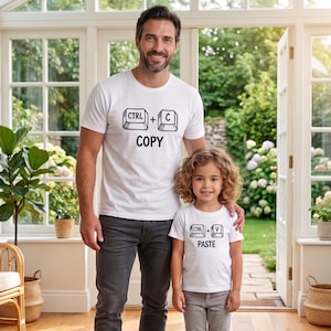 May include: Two white t-shirts with black text and graphics. One shirt says "CTRL + C COPY" and the other says "CTRL + V PASTE". A man and a child are wearing the shirts.