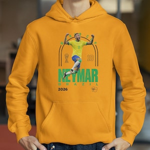 A yellow hoodie with a graphic of a soccer player in mid-jump, celebrating, and the text "NEYMAR BRASIL" and "2026" printed on it.
