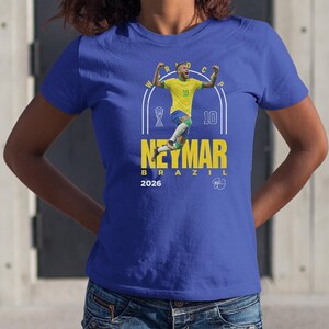 A person wearing a blue t-shirt with a graphic design featuring a soccer player in a yellow jersey and the text "Neymar Brazil 2026".