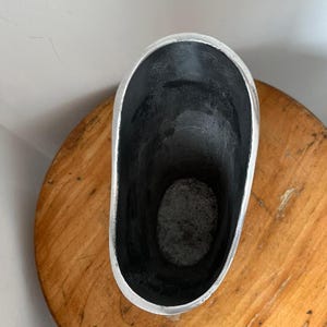 Pu&ograve; includere: Un contenitore argentato di forma ovale con un interno scuro. Il contenitore ha una finitura metallica liscia all'esterno e poggia su una superficie di legno. L'interno sembra essere di una tonalit&agrave; pi&ugrave; scura, forse nera.